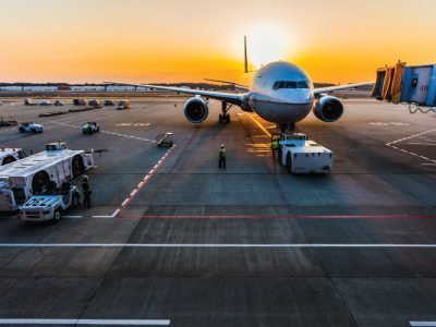 7-plzolkb8afco93fjq1a3tgvitrm4us1o0g10vec5a0 Airplane at airport gate during sunset with ground vehicles nearby.